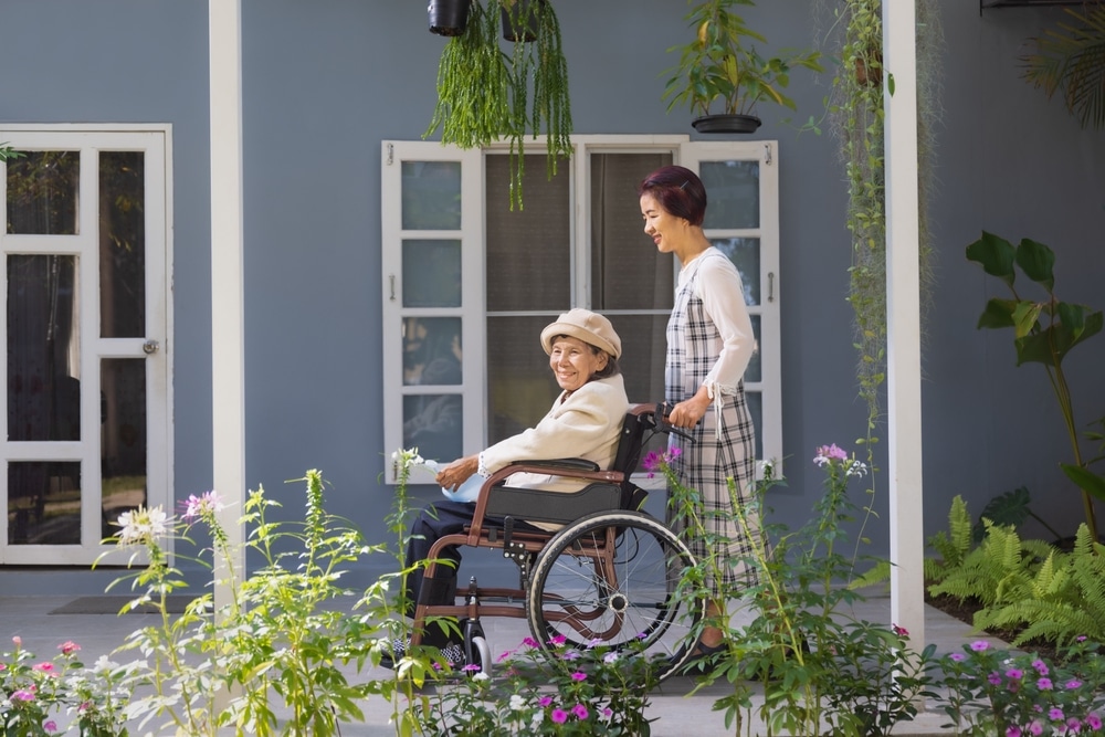 A woman pushes an older lady on a wheelchair in the garden.