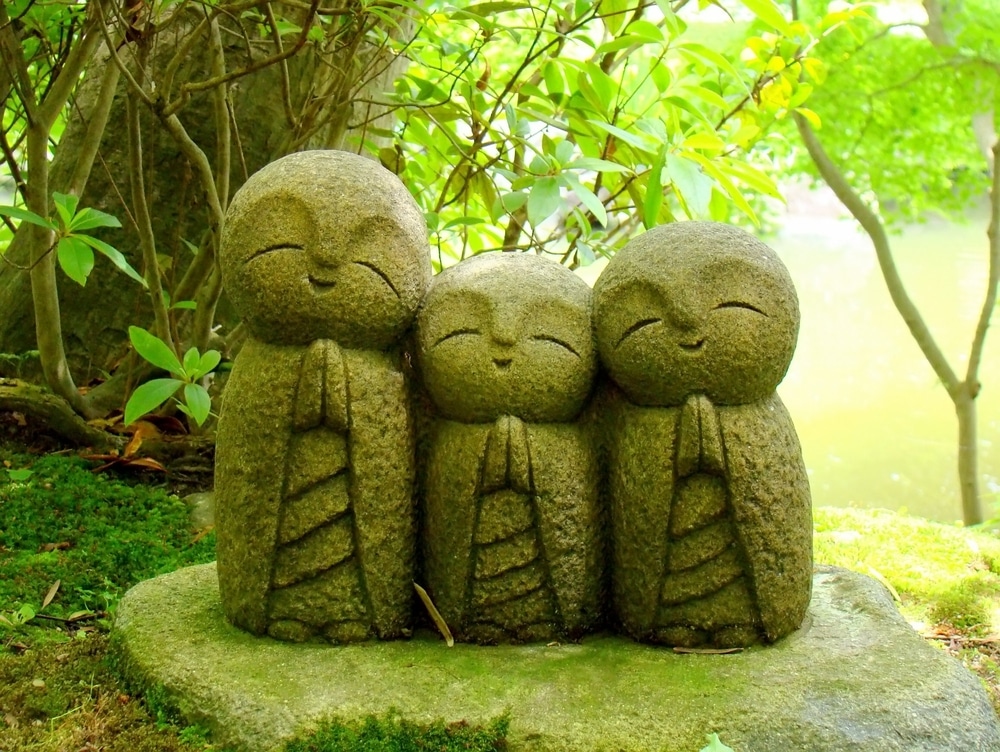 Three statues in a japanese garden with moss in the background