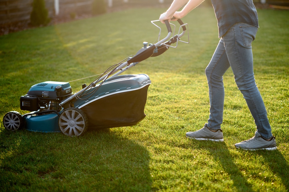 A man pushing a lawn mower in the early morning.