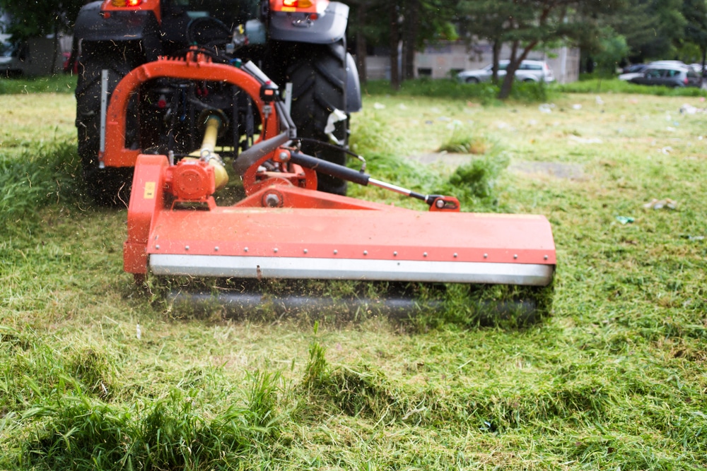 A red tow behind lawn mower is cutting grass as it is tugged along.